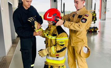 Strażacy ubierają dziecku w stroju strażackim kask.